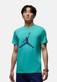 T-shirt in cotone turchese con un grande profilo silhouette del logo Jordan in blu navy sulla parte anteriore. Design a maniche corte e colletto rotondo.