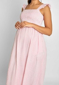 Rosa rutigt klänning med en smockad bodice, volangärmar och en flödande kjol, tillverkad av lättviktig bomullstyg.