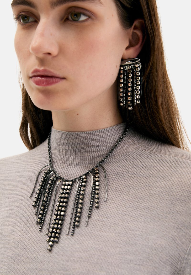 Smykkesæt i sort og sølv med en lang, frynset halskæde og matchende øreringe med rektangulære accenter og metallisk finish.