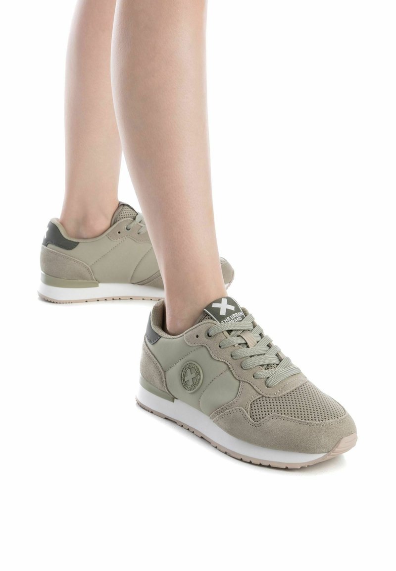 Zapatillas deportivas de color verde claro que presentan una mezcla de materiales de malla y ante, punta redondeada, diseño de cordones y acentos con patrones en los laterales.