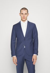 Navy blue suit with a tailored fit, single button closure, and notch lapels; paired with a white dress shirt and subtle shiny accents.