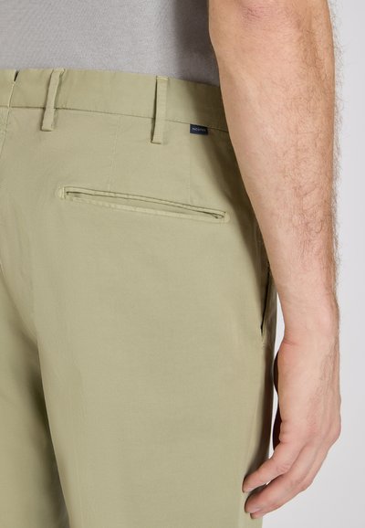 Beige pants with a back welt pocket and belt loops worn with a light gray shirt, showing part of a person's right hand and forearm.