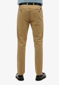 Khaki broek met een slim fit, duurzaam materiaal, twee achterzakken met knopen en minimale kreukels. Gemaakt in combinatie met zwarte schoenen.