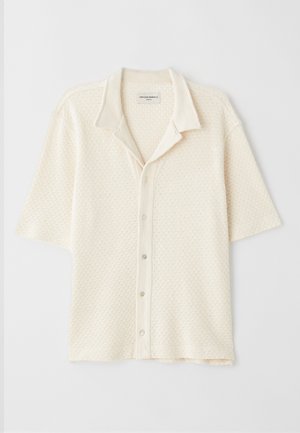 Camisa de manga corta con cuello en color crema, tejido texturizado con patrones de diamante, cierre de cinco botones y un corte relajado.
