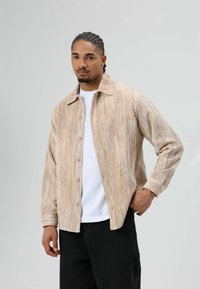 Lichtbruin corduroy overhemd met verticale strepen, lange mouwen, knoopsluiting aan de voorkant en een klassieke kraag, gedragen over een wit T-shirt.