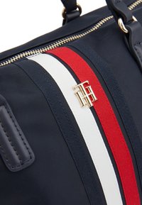 Borsa in nylon blu navy con design a strisce rosso, bianco e blu, logo in tonalità dorata, chiusura con zip e finiture in pelle con manici.