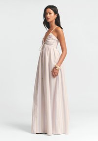 Maxi dress in light fabric with vertical pastel stripes, featuring adjustable spaghetti straps and a gathered bust detail.