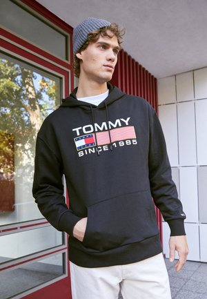 Felpa nera con un design grafico che presenta la scritta "TOMMY" e strisce rosse, blu e gialle. Dotata di tasca a marsupio e cappuccio con cordino.