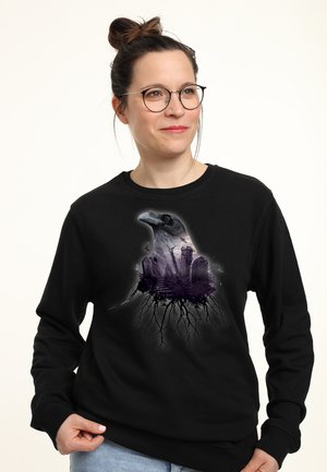 Černá mikina s potiskem grafiky hlavy havrana, která zahrnuje krajinu a kořeny, tištěná v odstínech šedé a fialové.