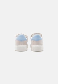 Ζευγάρι μπεζ σουέντ αθλητικά παπούτσια με γαλάζιες ταμπελίτσες στη φτέρνα, εμφανιζόμενα από πίσω, σε λευκό φόντο.