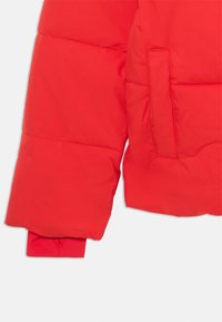 Manica di giacca imbottita rossa con una texture liscia e lucida, caratterizzata da un dettaglio della tasca cucita e polsini elasticizzati per una vestibilità aderente.