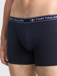 Mann trägt navyblaue Tom Tailor Boxershorts, sichtbar ist der Logo-Gummibund sowie ein Teil des Oberkörpers und der Oberschenkel.