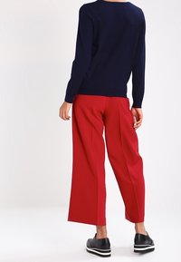 Marinblå stickad tröja med långa ärmar kombinerad med högmidjade, vida röda byxor och svarta platåskor. Dubbel texturdetalj synlig.
