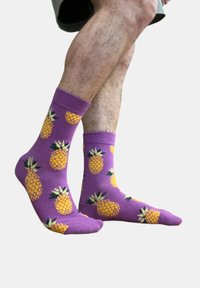 Chaussettes en coton violettes avec un motif ananas sur toute la surface, en jaune et vert. Longueur cheville avec un bord côtelé pour le confort.