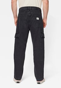 Pantaloni cargo neri in cotone, dotati di due tasche laterali con pattina, due tasche posteriori e una vestibilità rilassata con gamba dritta.