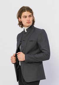 Donkergrijze blazer met een hoge kraag, een enkelvoudig design en subtiele stiksels. Bevat een ritszak en traditionele knopen.