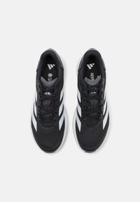 Baskets de sport noires avec tige en mesh, boîte à orteils texturée et trois bandes blanches sur les côtés. Comprend des lacets ronds et une semelle rembourrée.