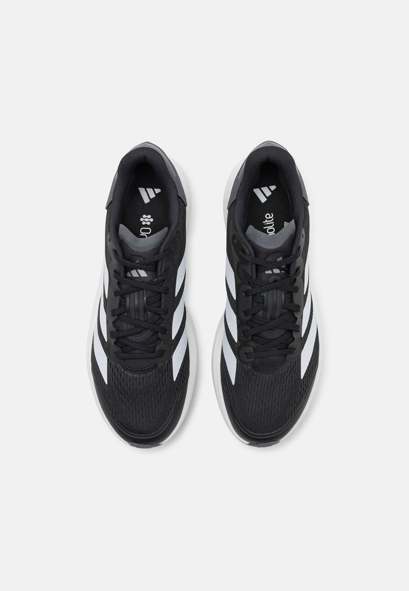 Zapatillas deportivas negras con parte superior de malla, puntera texturizada y tres rayas blancas en los lados. Presentan cordones redondos y suela acolchada.