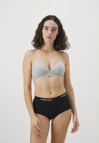 Világosszürke bralette vékony pántokkal és puha anyaggal, magasderekú fekete bugyival párosítva, amely fehér "PIECES" logós derékpánttal rendelkezik.