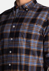 Overhemd met knopen in flanelstof, met een blauw-zwart geruit patroon en oranje accenten. Inclusief een borstzak en een knoopsluiting op de kraag.