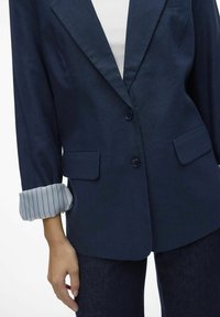 Merev navy bleiser, mis on valmistatud tekstuurses kangas, millel on kaks esikotti, lõikega krae ja üleskeeratud triibulised varrukad.