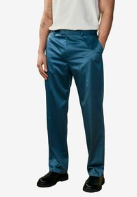 Teal-huurt haar pants, gemaakt van gladde stof, met een klassieke pasvorm en zakken, gecombineerd met zwarte schoenen en een lichtgekleurde top.