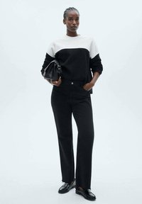 Black and white color-block sweater with long sleeves, paired with black straight-leg jeans and black loafers. Simple handbag accessory.