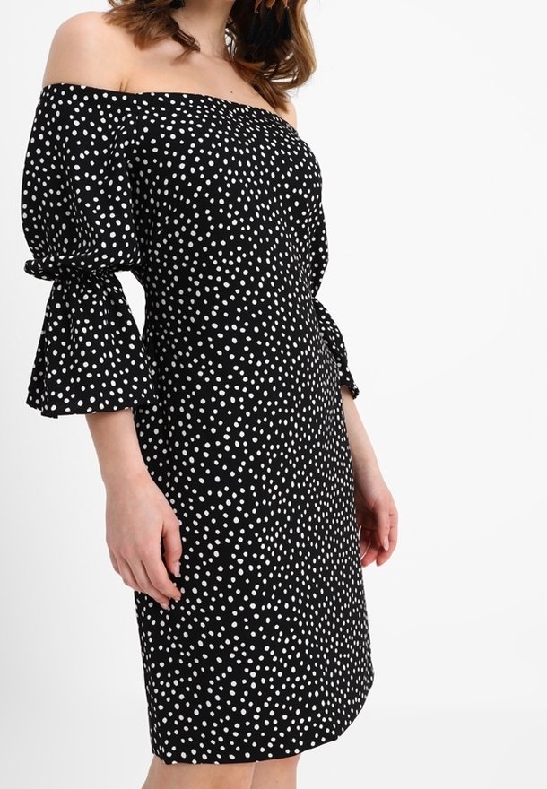 Svart off-shoulder klänning med vita prickar, med utsvängda ärmar och figurnära midja, tillverkad av lättviktsmaterial.