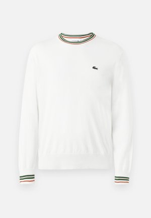 Pull blanc à col rond, avec des accents rayés verts, rouges et oranges sur le col et les manches. Logo Lacoste sur la poitrine.