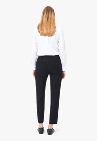 Svarta skräddarsydda byxor med slim fit, med två bakfickor och en jämn textur, kombinerade med en vit skjorta med knappar.