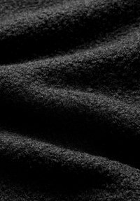 Gros plan d'un tissu en laine gris foncé texturé avec des plis doux créant des motifs de lumière et d'ombre.