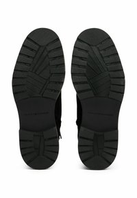 Soles of black Tommy Hilfiger boots with deep grooves and tread patterns for traction, displayed side by side on white background.