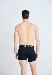 Sorte boxer shorts med en hvit "HILFIGER" logo på kanten, laget av et glatt, strekkbart materiale, vist fra baksiden.
