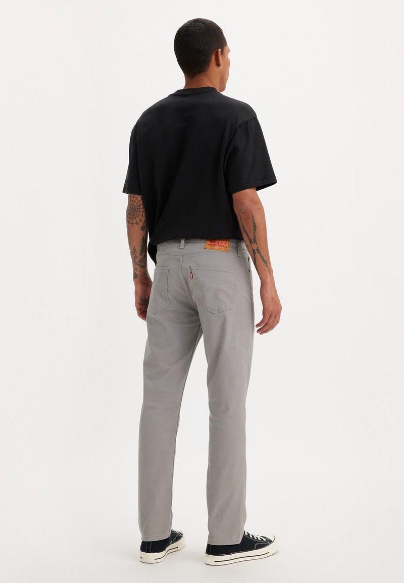 T-shirt noir à manches courtes, pantalon droit gris et baskets noires. Détails notables : une étiquette rouge Levi's sur la ceinture.