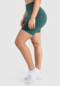 Pantaloni corto alti verdi senza cuciture con una texture liscia, caratterizzati da un design aderente. Abbinati a scarpe sportive bianche.