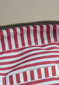 Interior de tejido a rayas rojas y blancas con una textura suave, que presenta un zipper a lo largo del borde. Rayas horizontales de diferentes anchos.