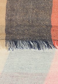 Vævet tekstil med et houndstooth mønster i mørkeblå, beige og koralfarvet med frynser. Teksturen fremstår blød og detaljeret.