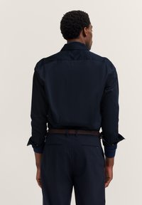 Navyblaues Hemd aus glattem Stoff, mit langen Ärmeln und geknöpften Manschetten, von hinten mit einem kontrastierenden Kragendetail präsentiert.