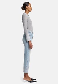 Maglione grigio a costine con maniche lunghe e colletto, abbinato a jeans azzurri chiari con decorazioni all'orlo, e décolleté neri a punta.