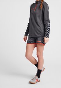 Sudadera deportiva gris oscuro con cremallera roja, pantalones cortos a juego con acentos rojos y mangas con patrón. Zapatillas grises y rojas completan el conjunto.