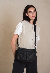Borsa a tracolla nera con due tasche frontali con zip, realizzata in materiale testurizzato. Presenta una tracolla regolabile e un design minimalista.