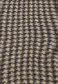 Tissu avec un motif pied-de-poule bleu marine et beige. La texture est tissée, présentant de petites formes géométriques distinctes réparties uniformément sur la surface.