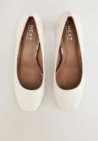 Zapatos planos blancos hechos de cuero suave, con un acabado texturizado sutil, puntera redondeada y un diseño sin cordones con una plantilla acolchada.