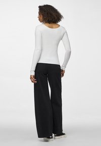 Bílé dlouhé rukávy žebrované tričko s kulatým výstřihem, spárované s širokými černými džínami a tmavými teniskami. Hladká textura a přiléhavý střih.