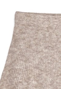 Stickad tyg i ljus beige med en texturerad mönstring, som har en ribbad midja. Ytan visar subtila variationer i färg och djup.