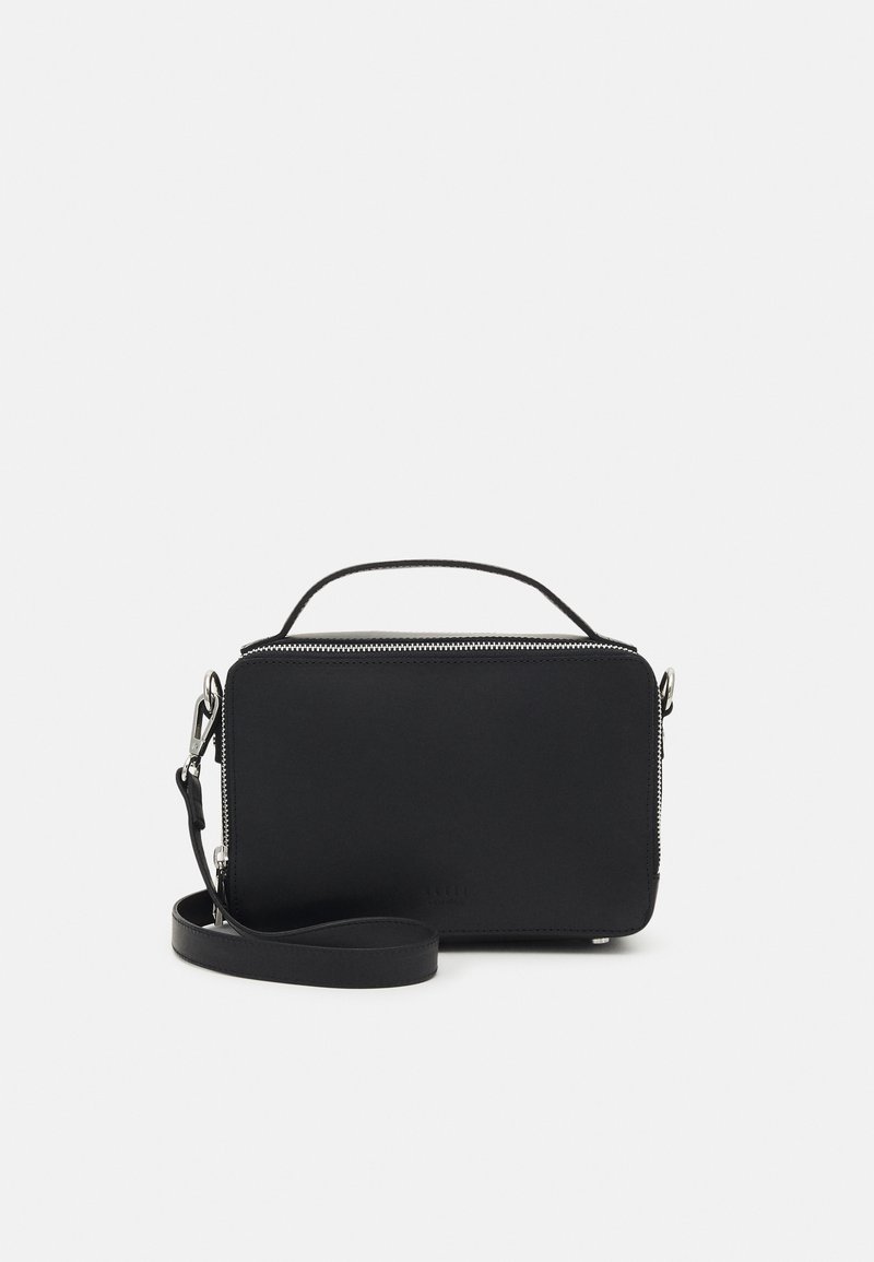 Sac bandoulière noir en simili cuir avec une fermeture éclair supérieure, un design plat, une anse courte et une sangle détachable. Présente des accents matériels minimaux.