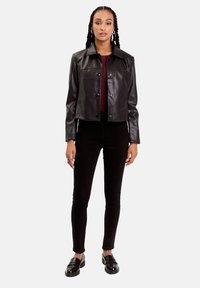 Veste en cuir noir coupée avec un col plat, des boutons sur le devant et des manches allongées, associée à un pantalon noir slim et des mocassins.