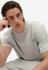 Hellgraues Baumwoll-T-Shirt mit kurzen Ärmeln und Rundhalsausschnitt, mit kleinem Logo auf der Brust. Glatte Textur, legerer Schnitt.