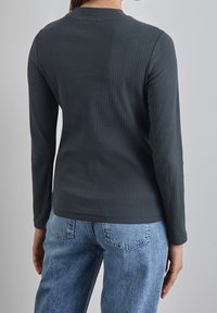 Mörkgrå ribbad långärmad topp med rund halsringning, i kombination med ljusblå högmidjade jeans. Detaljerad rygg med textilmaterial.