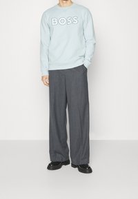 Ljusblå sweatshirt med "BOSS"-logo, i kombination med mörkgrå vida byxor och svarta klumpiga skor. Släta texturer, avslappnad passform.